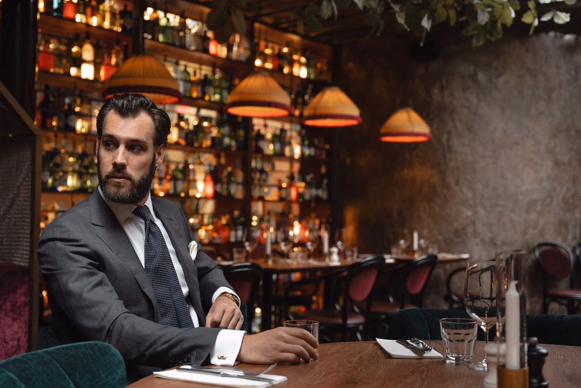 Man in a grey suit and dotted tie seated in a warmly lit bar